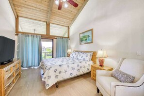 A bedroom with a bed, a television, a chair, a nightstand, and a ceiling fan.