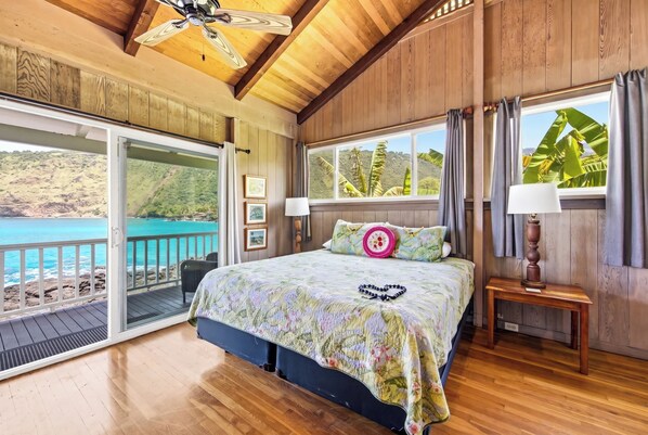 Une chambre avec un grand lit, un plafond en bois, une vue sur l’océan et un balcon.