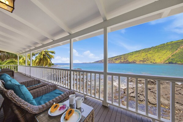 A covered outdoor seating area with a view of the ocean and a hillside.