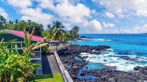 A coastal property with a red-roofed building, a rocky shoreline, and a clear blue ocean.
