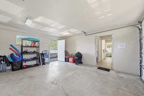 A garage with a concrete floor, a door leading to a bedroom, and various sports equipment stored on shelves. - *NEW* Kealakekua Bay Oceanfront Home with Views from Every Room (Captain Cook)
