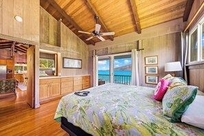 Een slaapkamer met een bed, een plafondventilator, houten wanden, uitzicht op de oceaan en een balkon.