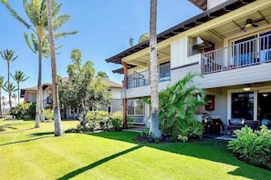 Ein zweistöckiges Haus mit Balkon, Rasen und Palmen.