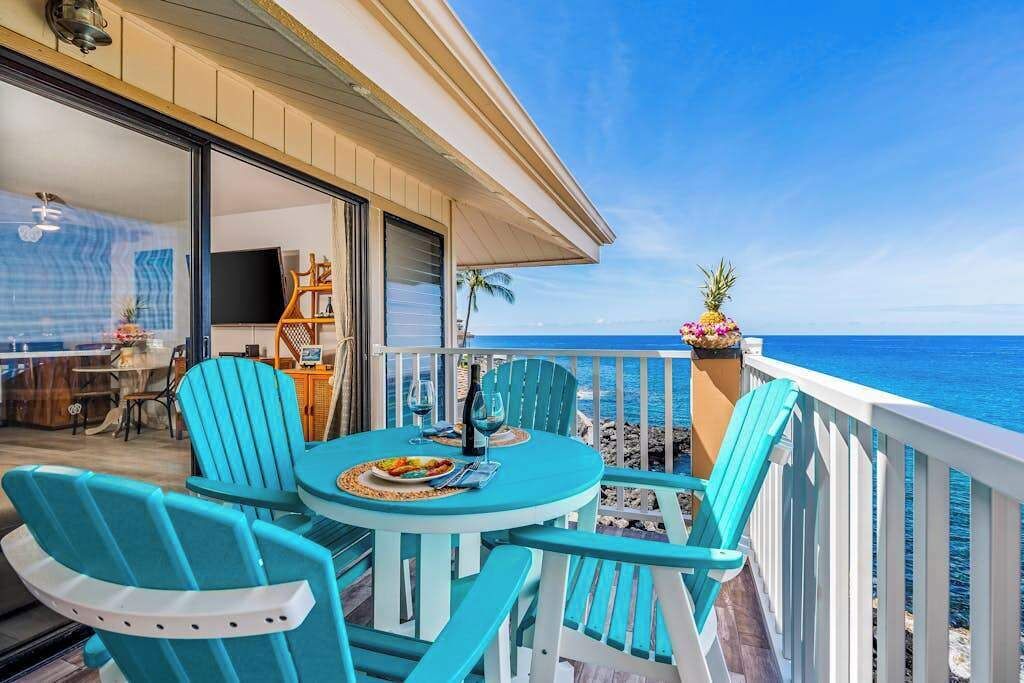 Un balcon avec des chaises turquoise et une table, donnant sur l’océan.