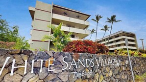 Un mur de pierres sur lequel est inscrit le texte « WHITE SANDS VILLAGE » et un numéro de téléphone.