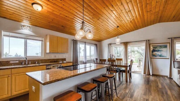 Una cocina con techo de madera, una isla central, taburetes de bar y un comedor con sillas.