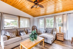 A spacious living room with a wooden ceiling, large windows, a sofa set, a coffee table, and a side table with a lamp. - *NEW* Pacific-View Waikoloa Home Near Golf and Beach Days (Waikoloa Village)