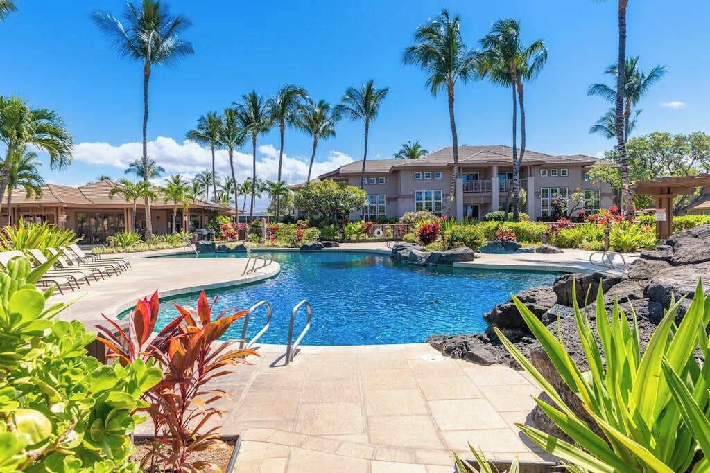 A resort with a swimming pool, palm trees, and a building with multiple balconies.
