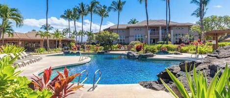 A resort with a swimming pool, palm trees, and a building with multiple balconies.