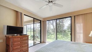 Ein Schlafzimmer mit einem Bett, einem Fernseher auf einer Kommode und einer Glasschiebetür, die auf einen Balkon führt.