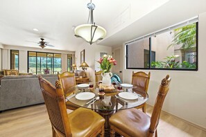 Uma sala de jantar com mesa de vidro, cadeiras de madeira e um vaso de flores.