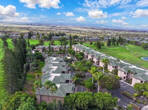 Un quartier résidentiel composé de plusieurs maisons à deux étages, d’un terrain de golf et d’un grand bâtiment visible au loin.