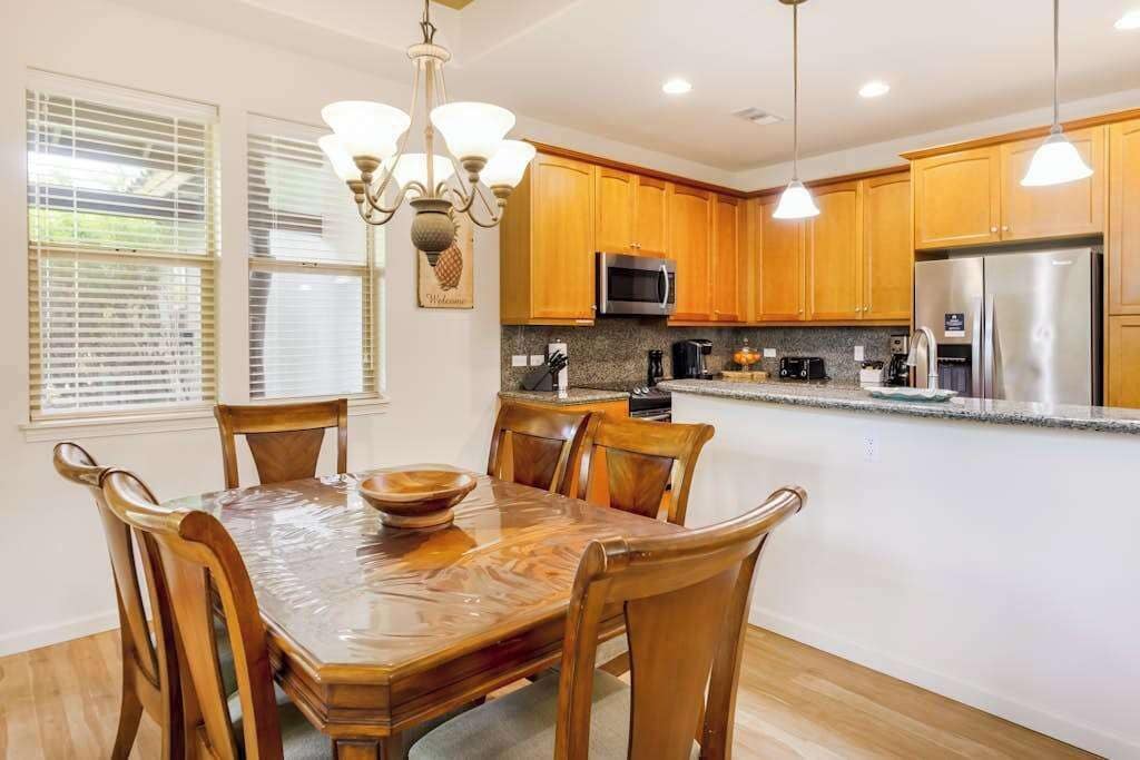 A kitchen with wooden cabinets, a stainless steel refrigerator, a microwave, and a dining table with chairs.