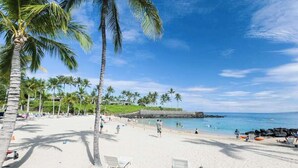 Una spiaggia con palme, un litorale roccioso e un cielo azzurro limpido.