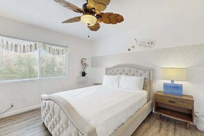 A bedroom with a bed, a nightstand, a lamp, a ceiling fan, and a window with blinds. - NEW Fall Sale Private Waikoloa Home with Coastal Views and Hot Tub (Waikoloa Village)