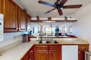 A kitchen with wooden cabinets, a ceiling fan, a dishwasher, and a large window. - *New* Fall Special Ocean and Golf Views from a Kona Lanai for Four (Kailua-Kona)