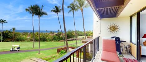 A balcony with a view of a golf course, palm trees, and the ocean.