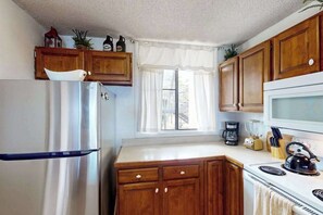 A kitchen with wooden cabinets, a refrigerator, a microwave, and a stove. - *New* Fall Special Ocean and Golf Views from a Kona Lanai for Four (Kailua-Kona)
