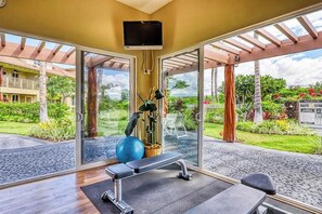 A gym with exercise equipment, a television, and large glass doors leading to a garden. - Waikoloa Beach Resort Villa-Golf, Pools, Hot Tub, Local Shops, Dining, Beach Fun (Waikoloa)