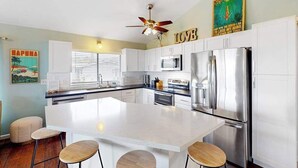 Une cuisine moderne avec des meubles blancs, un îlot central, des appareils en acier inoxydable et un ventilateur de plafond.