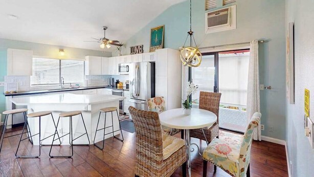Une cuisine moderne avec un îlot central, des tabourets de bar, des chaises en osier et une table à manger.
