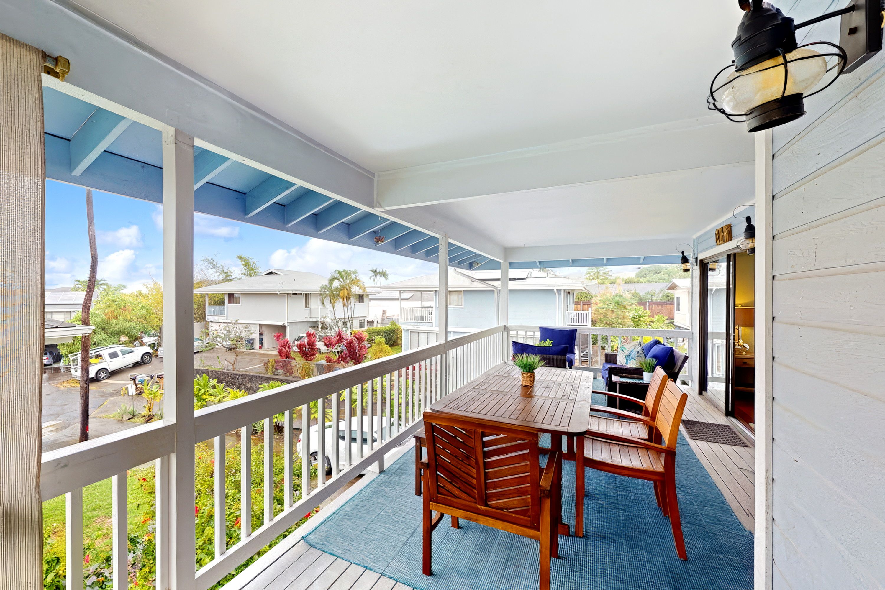 A covered outdoor area with a table and chairs, a railing, and a view of the neighborhood.