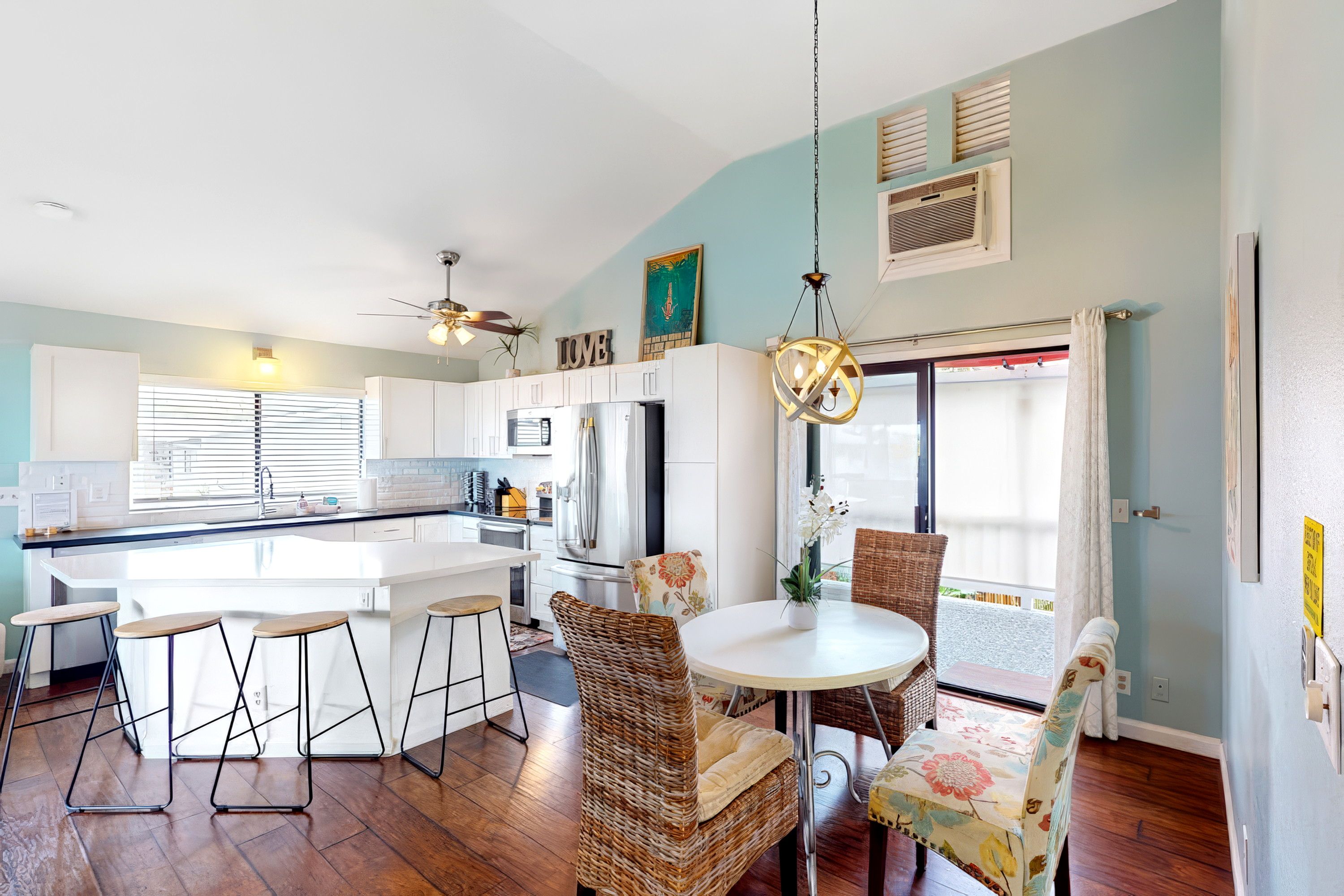 A modern kitchen with a central island, bar stools, and a dining area with wicker chairs.