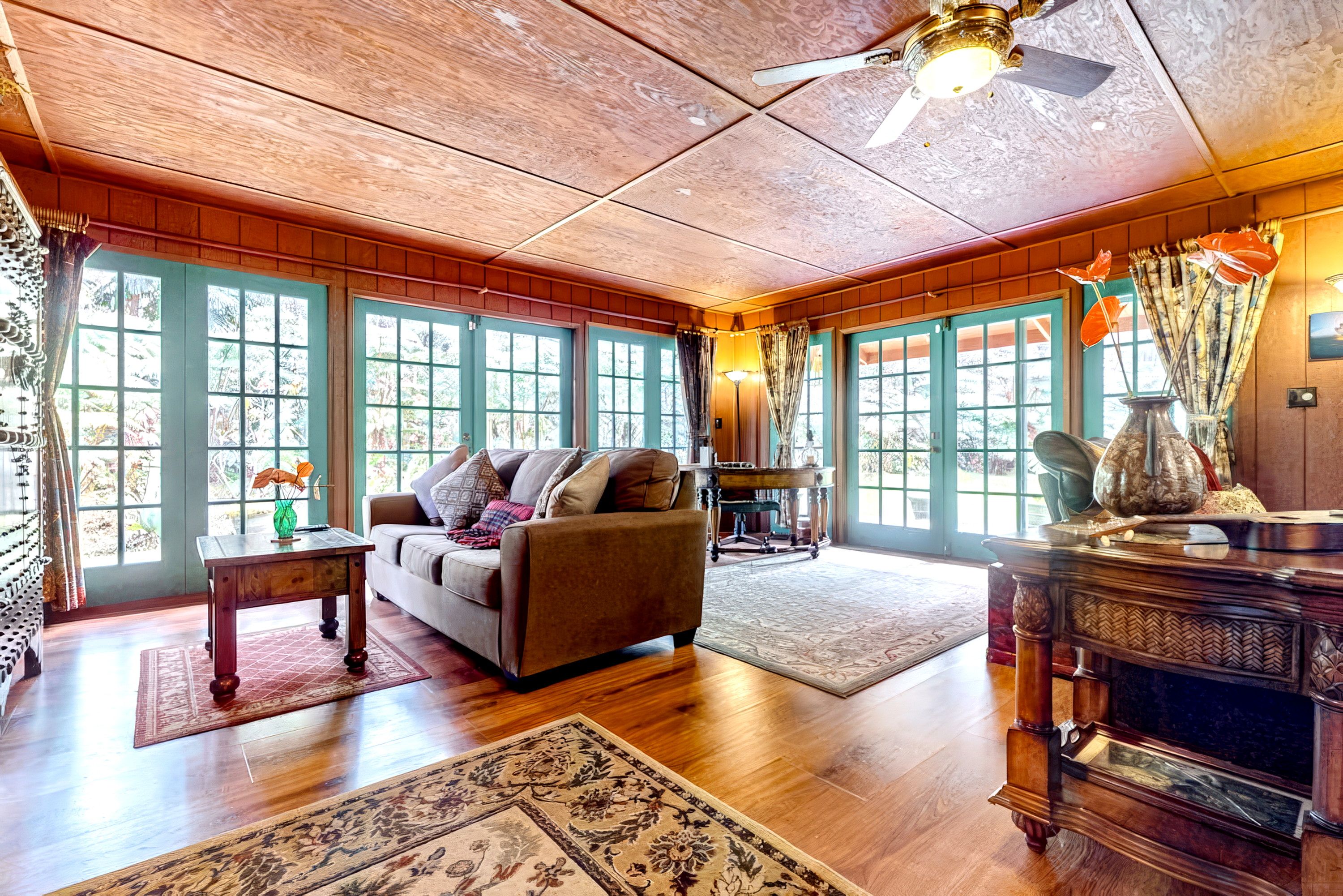 A spacious room with a wooden ceiling, large windows, a sofa, a table, and a decorative vase.