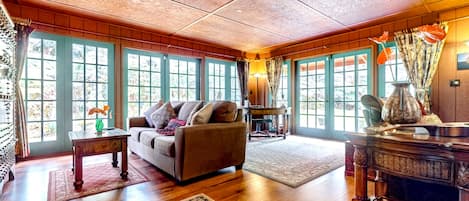 A spacious room with a wooden ceiling, large windows, a sofa, a table, and a decorative vase.