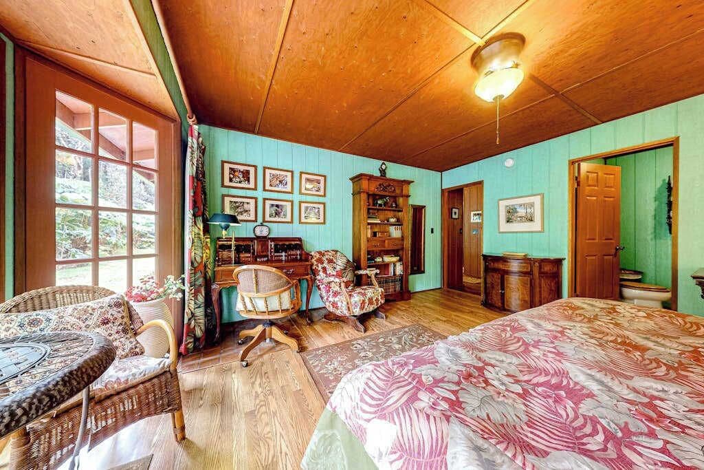 A room with a bed, wicker chairs, a wooden desk, and a bookshelf.