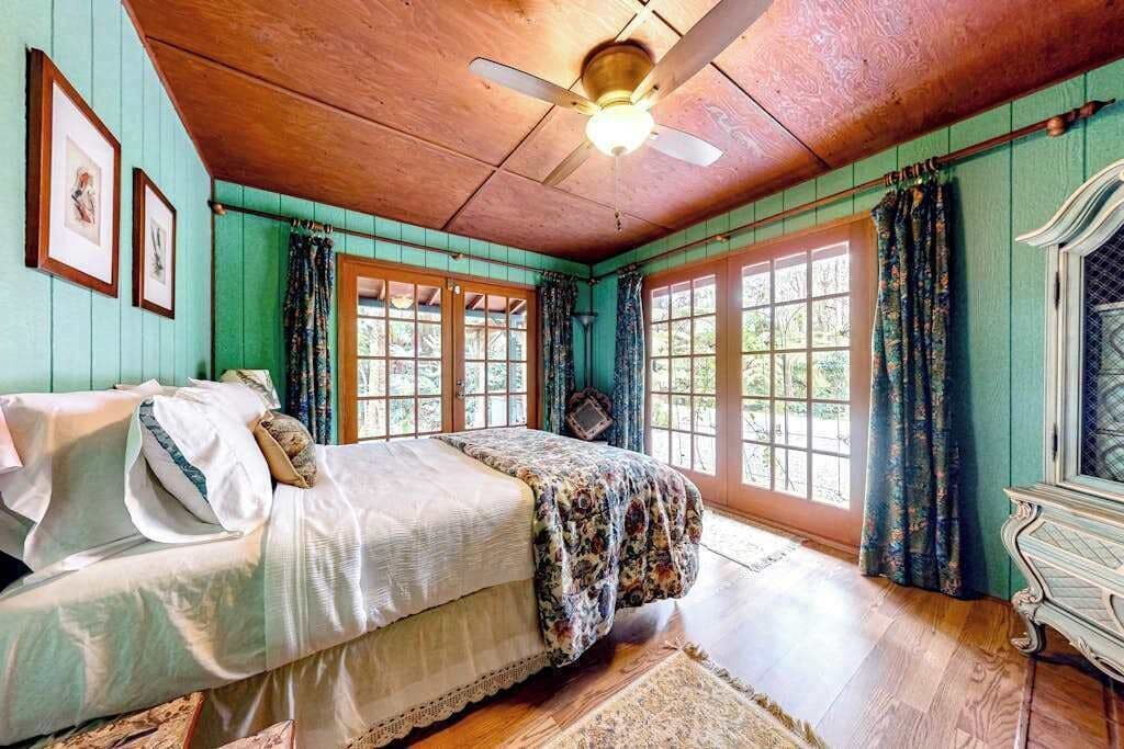 A bedroom with a bed, a ceiling fan, and large windows.