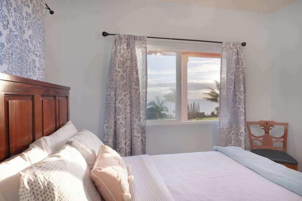 Una camera da letto con una testiera in legno, un letto con biancheria bianca, una finestra con tende e vista sull'esterno.