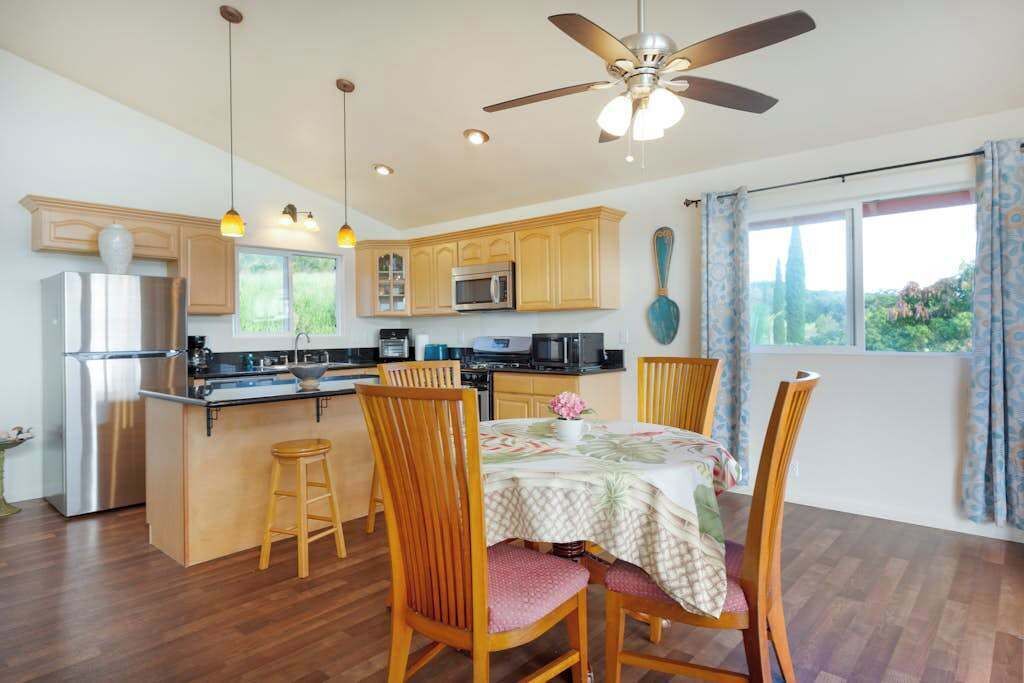 A modern kitchen with wooden cabinets, a stainless steel refrigerator, and a dining area with wooden chairs and a table.