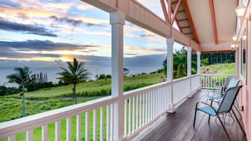 A covered porch with a view of the sea and a grassy landscape.