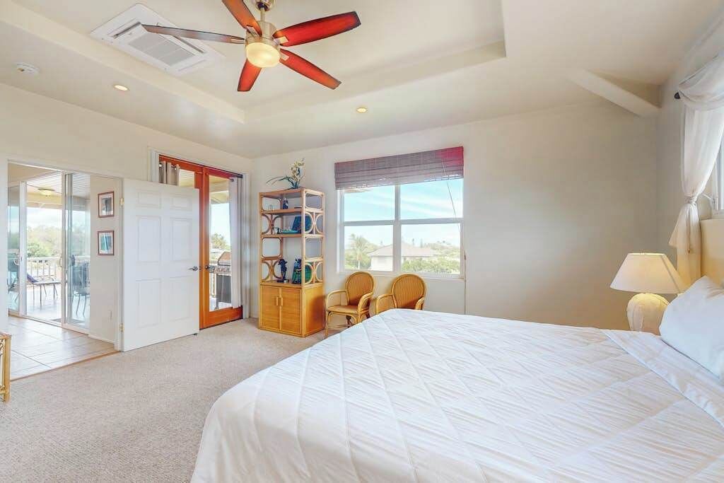 A bedroom with a bed, a ceiling fan, a window with curtains, a bookshelf, and a door leading to a balcony.