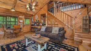 A wooden cabin interior with a dining area, a sofa, a staircase, and a kitchen. - Bears in the Mist (Sevierville)