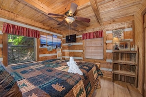 A wooden cabin bedroom with a bed, ceiling fan, TV, and large windows. - Bears in the Mist (Sevierville)