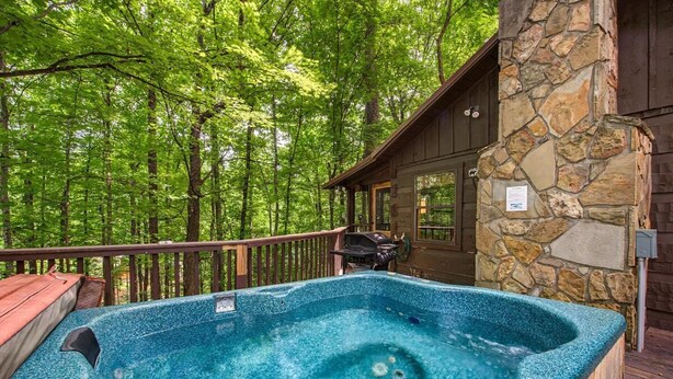 A hot tub on a wooden deck with a stone wall and a wooden cabin in the background. - Bears in the Mist (Sevierville)