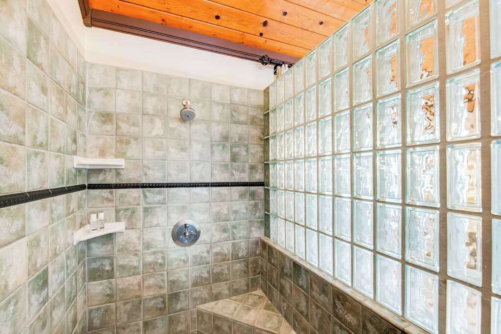 A shower with a wooden ceiling, tiled walls, and a glass block wall.