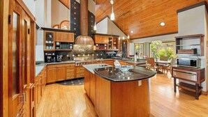 A spacious kitchen with wooden cabinets, a central island, and a large stove. - NEW Fall Sale Private Infinity Pool Above Kona Coffee Country (Captain Cook)
