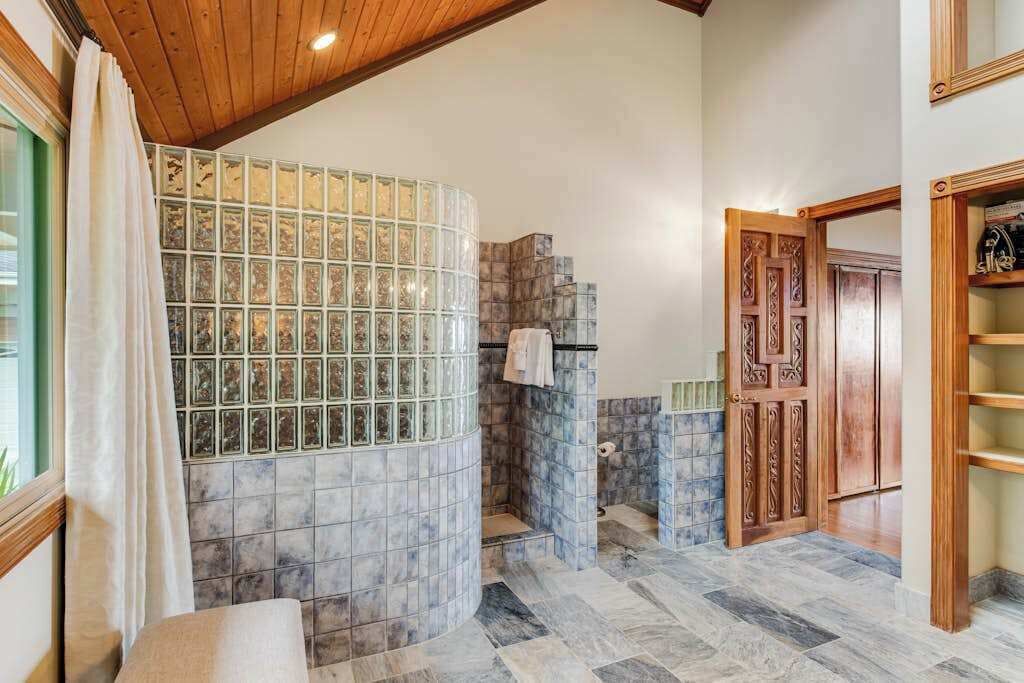 A bathroom with a glass shower enclosure, tiled walls, a wooden door, and a bench.