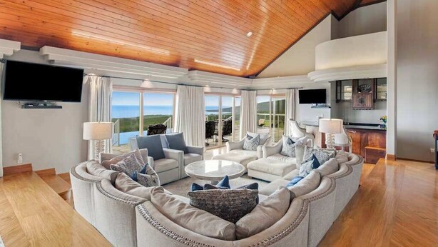 A spacious living room with a curved sofa, a coffee table, and a flat-screen TV mounted on the wall. - NEW Fall Sale Private Infinity Pool Above Kona Coffee Country (Captain Cook)