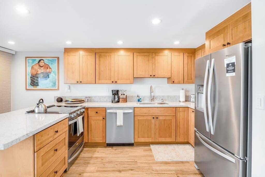 Una cocina moderna con armarios de madera, electrodomésticos de acero inoxidable y un cuadro en la pared.