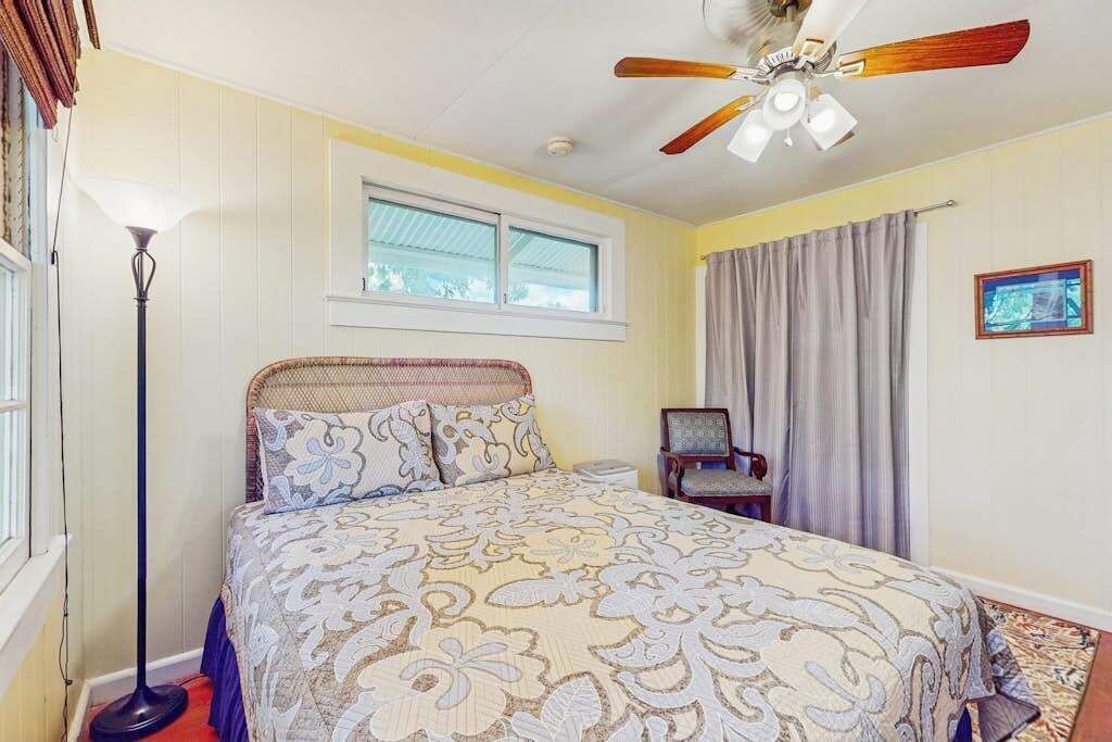 Ein Schlafzimmer mit Bett, Deckenventilator, Stehlampe, Sessel und Fenster.