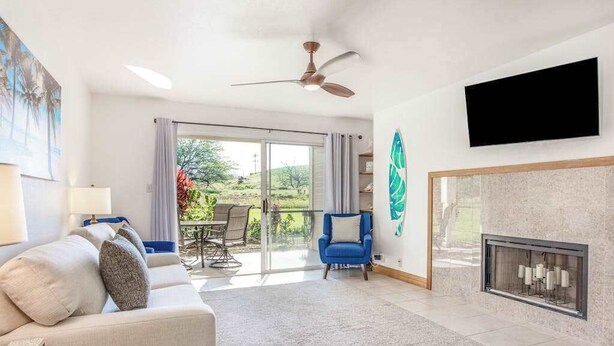 Un salon moderne avec un canapé, un fauteuil bleu, une cheminée et un téléviseur fixé au mur.