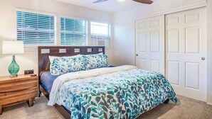 Une chambre à coucher comprenant un lit, une table de chevet, une lampe, un ventilateur de plafond et une fenêtre avec des stores.
