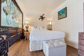 Ein Hotelzimmer mit einem großen Bett, Holzboden, einem Vogelgemälde, einer Schildkröten-Wanddekoration und einer Lampe.