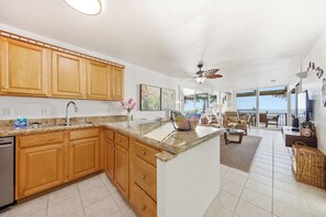 A kitchen with wooden cabinets, a granite countertop, and a dining area with a view. - Beachfront Kona Bali Kai 302 at Holualoa Bay-Pool, Hot Tub, Laundry, Lanai, WIFI (Kailua-Kona)