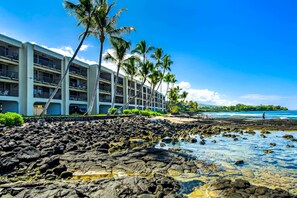 A hotel with multiple floors, a rocky shoreline, and palm trees. - Beachfront Kona Bali Kai 302 at Holualoa Bay-Pool, Hot Tub, Laundry, Lanai, WIFI (Kailua-Kona)