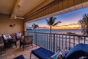 Ein Balkon mit Blick auf das Meer bei Sonnenuntergang, ausgestattet mit einer Sitzecke inklusive Stühle und Tisch.